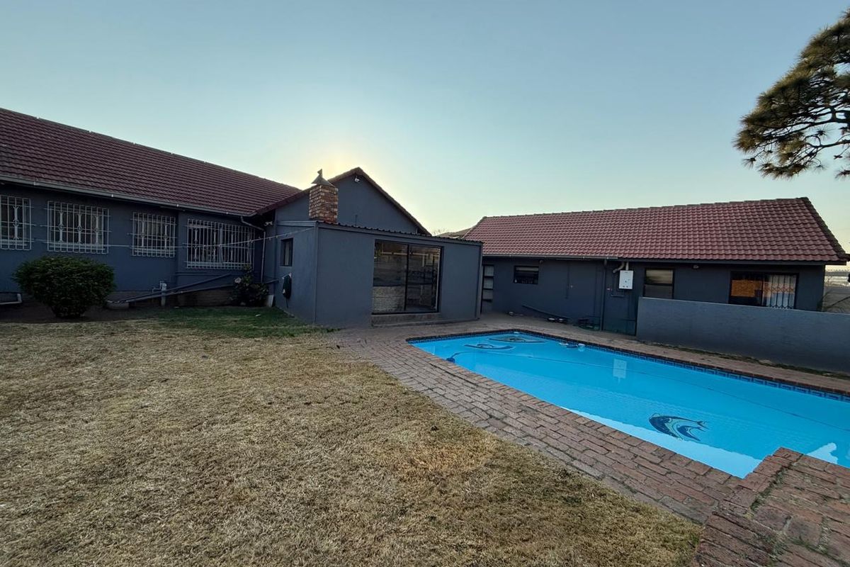 Rear exterior view of the property featuring a swimming pool, brick paved surround, and a large lawn area.