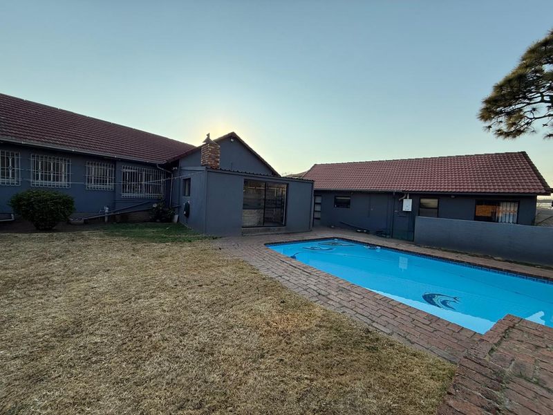 Rear exterior view of the property featuring a swimming pool, brick paved surround, and a large lawn area.