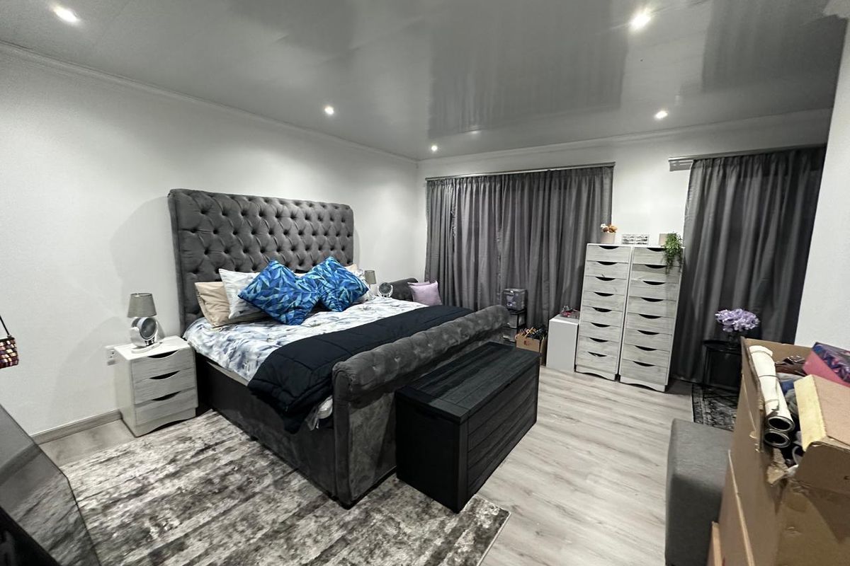 A spacious bedroom featuring modern laminate flooring, recessed downlighting, and a high-gloss ceiling finish.