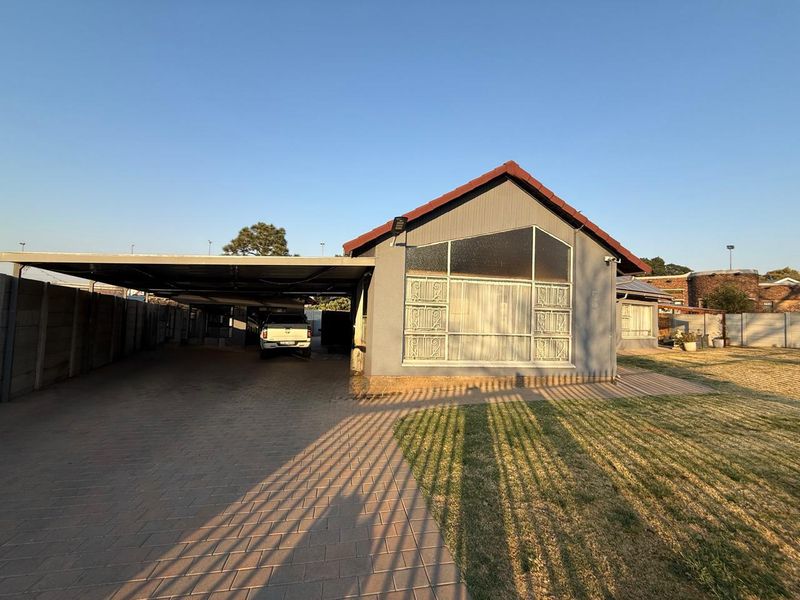 Front elevation of the house featuring a large paved driveway, an attached carport, and security-fitted windows.