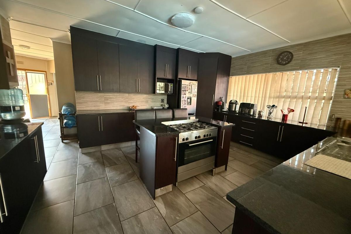 Spacious kitchen featuring dark wood cabinetry, granite countertops, a central island with a gas stove, and large format floor tiles.