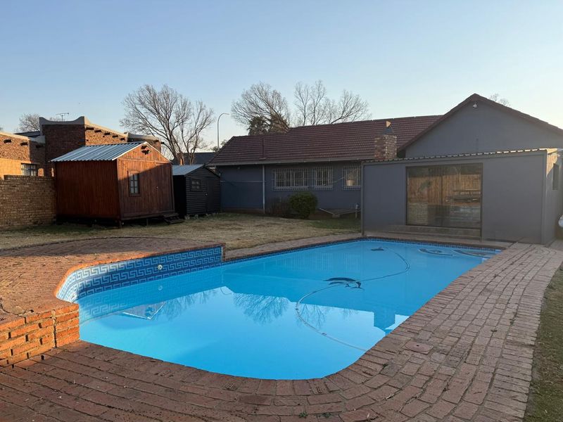 Rear garden area featuring a swimming pool with brick paving surround and a view of the main house exterior.