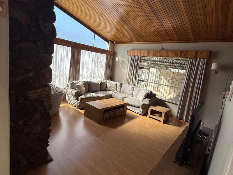 Spacious living room featuring a striking stone fireplace, high vaulted timber ceilings, and large windows that provide ample natural light.