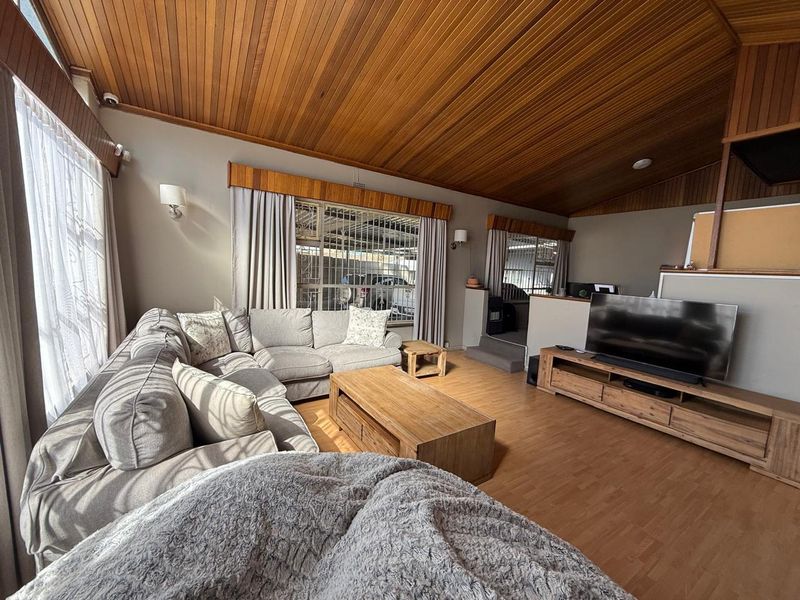 Spacious living room featuring a distinctive timber-clad vaulted ceiling, laminate flooring, and large windows fitted with security bars.