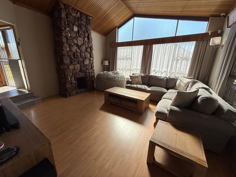 Spacious living room featuring a striking stone fireplace, vaulted timber ceilings, and large windows that provide ample natural light.