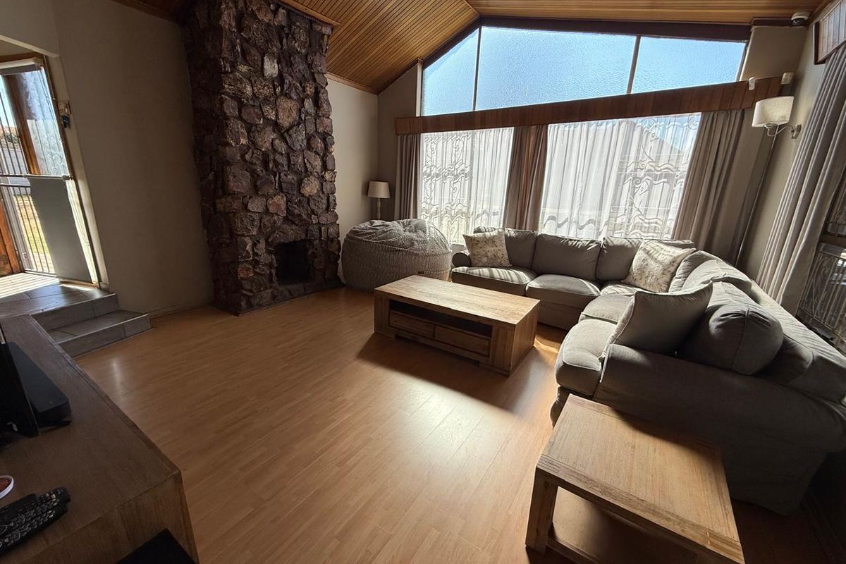 Spacious living room featuring a striking stone fireplace, vaulted timber ceilings, and large windows that provide ample natural light.
