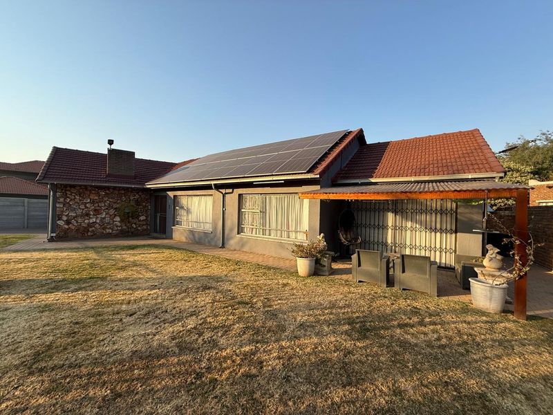 Rear view of the house featuring a tiled roof with solar panels, stone cladding accents, and a covered patio area overlooking the garden.