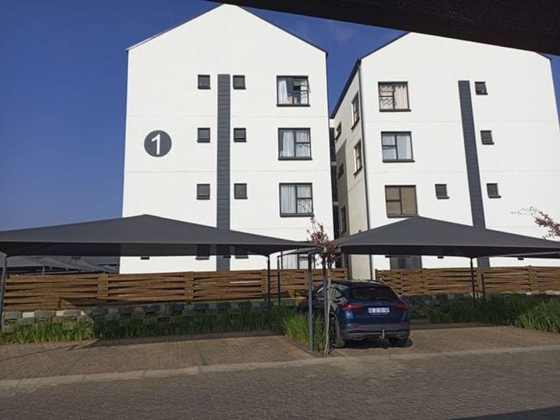 Exterior view of a modern multi-story apartment building featuring dedicated shade cloth parking bays and paved driveway access.