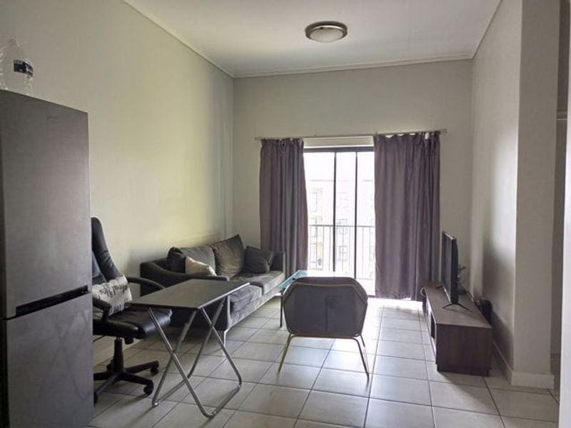 A living room featuring tiled flooring and a sliding glass door leading to a balcony, providing natural light to the space.