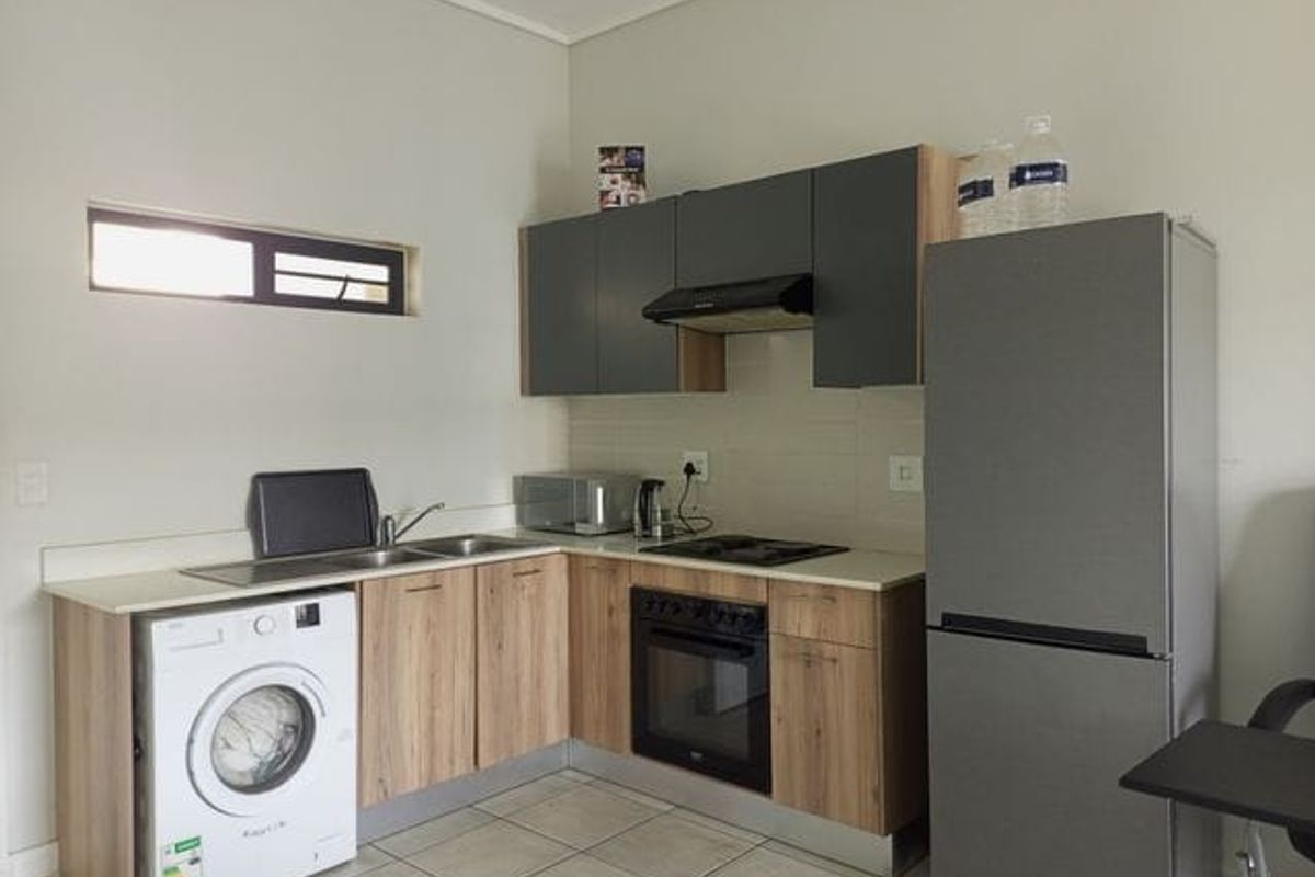 A functional kitchen featuring modern wood-finish cabinetry, integrated oven and hob, tiled backsplash, and dedicated space for a washing machine.