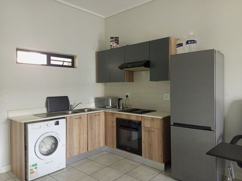A functional kitchen featuring modern wood-finish cabinetry, integrated oven and hob, tiled backsplash, and dedicated space for a washing machine.