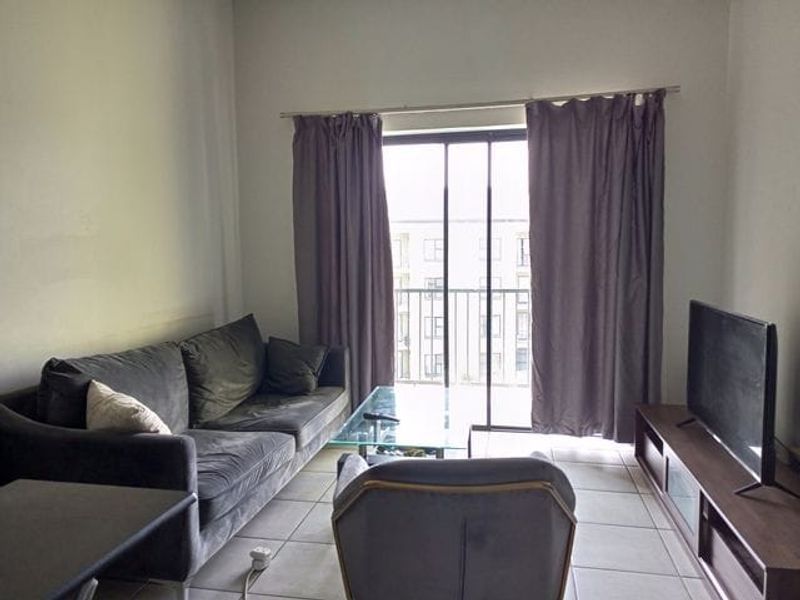 A living room featuring tiled flooring and a sliding glass door that opens to a balcony, providing natural light to the space.