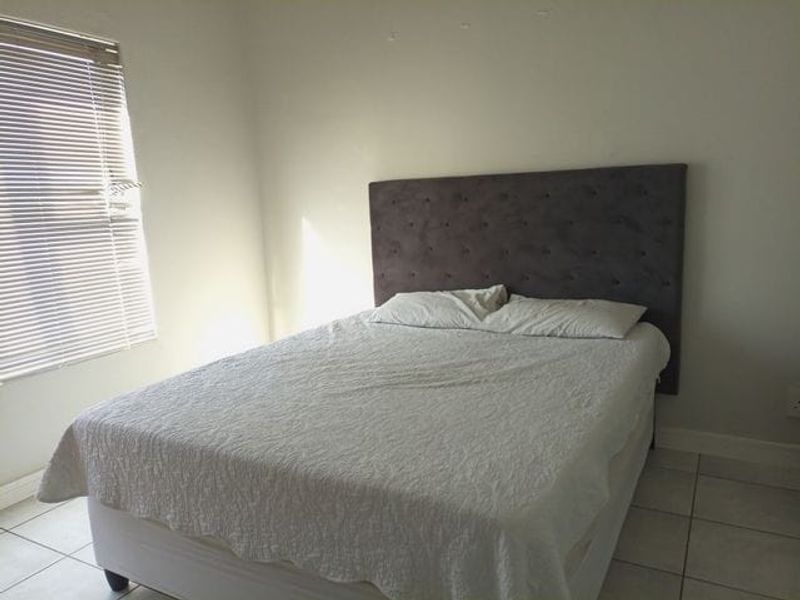 A simple bedroom featuring tiled flooring and venetian blinds, providing a functional and neutral space.