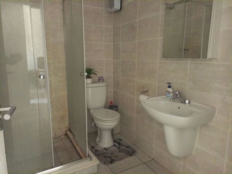 A functional bathroom featuring a glass shower enclosure, pedestal basin, toilet, and wall-mounted mirror cabinet with neutral wall and floor tiling.