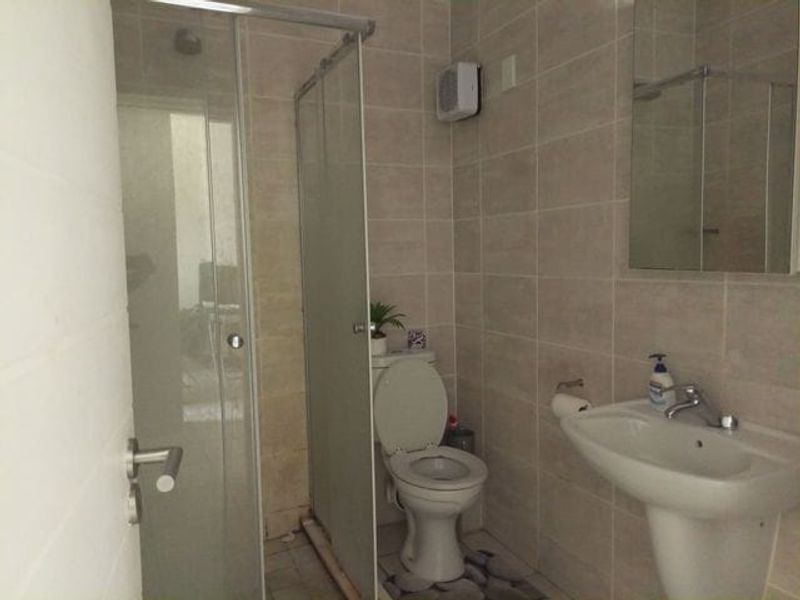 A functional bathroom featuring a glass shower enclosure, pedestal sink, wall-mounted mirror, and neutral wall tiling.
