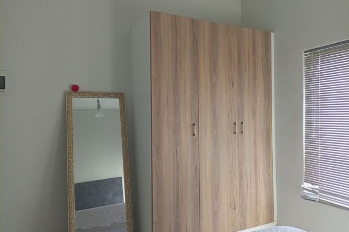 A bedroom featuring a modern wood-finish built-in wardrobe and window with venetian blinds.