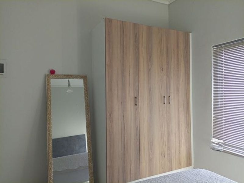A bedroom featuring a modern wood-finish built-in wardrobe and window with venetian blinds.