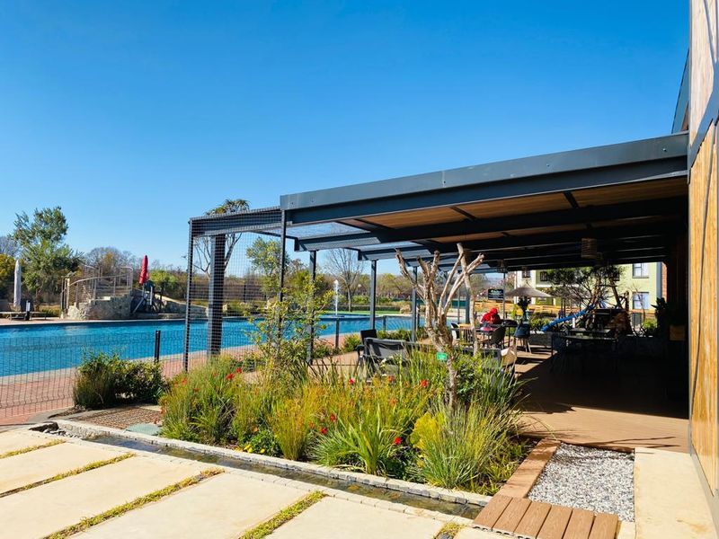 A well-maintained outdoor pool area featuring a covered patio, modern decking, landscaped garden beds, and a water feature, perfect for leisure and recreation.