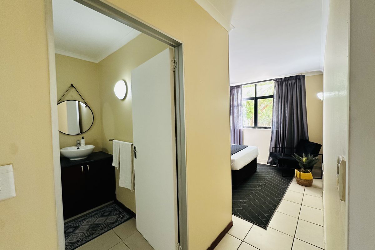 A bedroom featuring tiled flooring and an en-suite vanity area with a vessel sink and dark cabinetry.