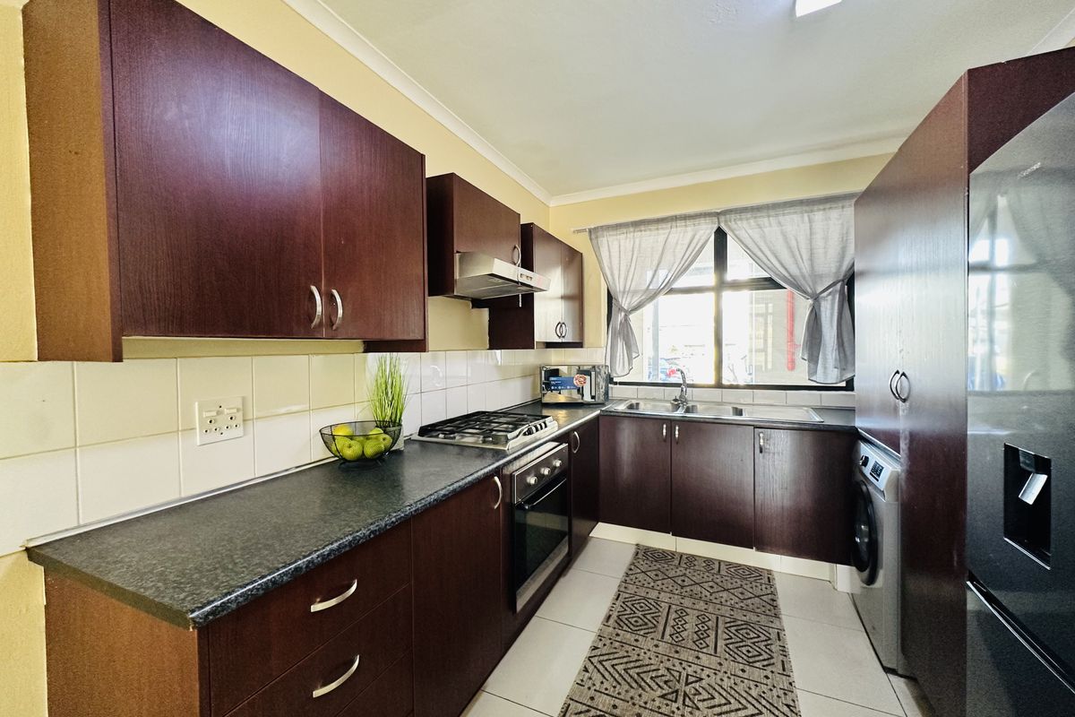 A functional kitchen featuring dark wood cabinetry, laminate countertops, a built-in oven with gas hob, and a double sink with tiled backsplash.