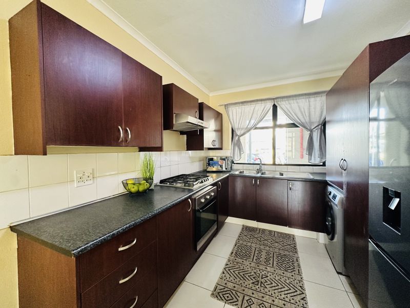 A functional kitchen featuring dark wood cabinetry, laminate countertops, a built-in oven with gas hob, and a double sink with tiled backsplash.