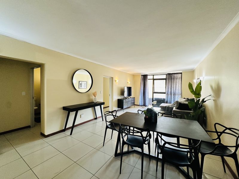 Spacious open-plan living and dining area featuring tiled flooring, neutral wall tones, and access to a balcony through a sliding glass door.