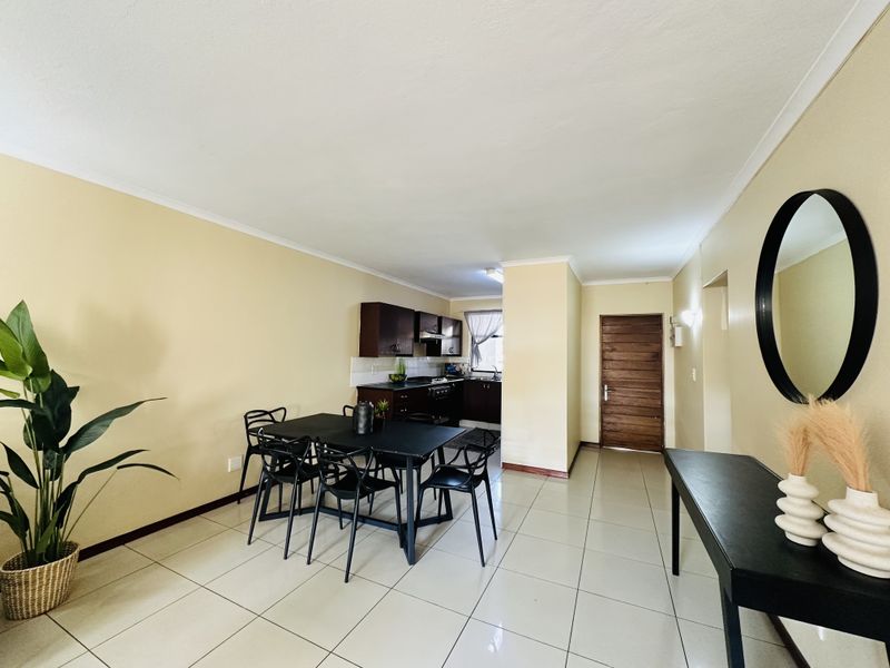 Open-plan living and dining area featuring tiled flooring and a compact kitchen with built-in cabinetry, hob, and extractor fan.