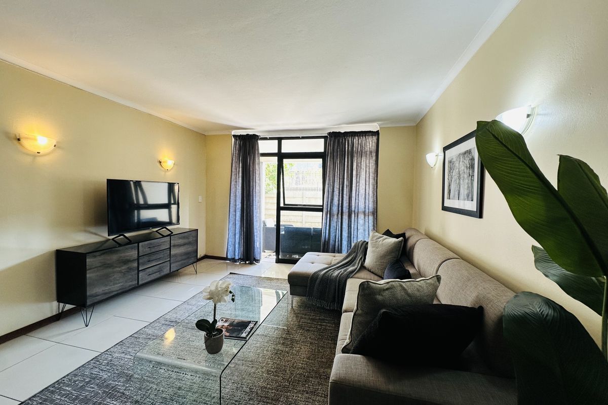 A well-lit living room featuring tiled flooring, wall-mounted lighting, and a sliding glass door providing access to the outdoor area.
