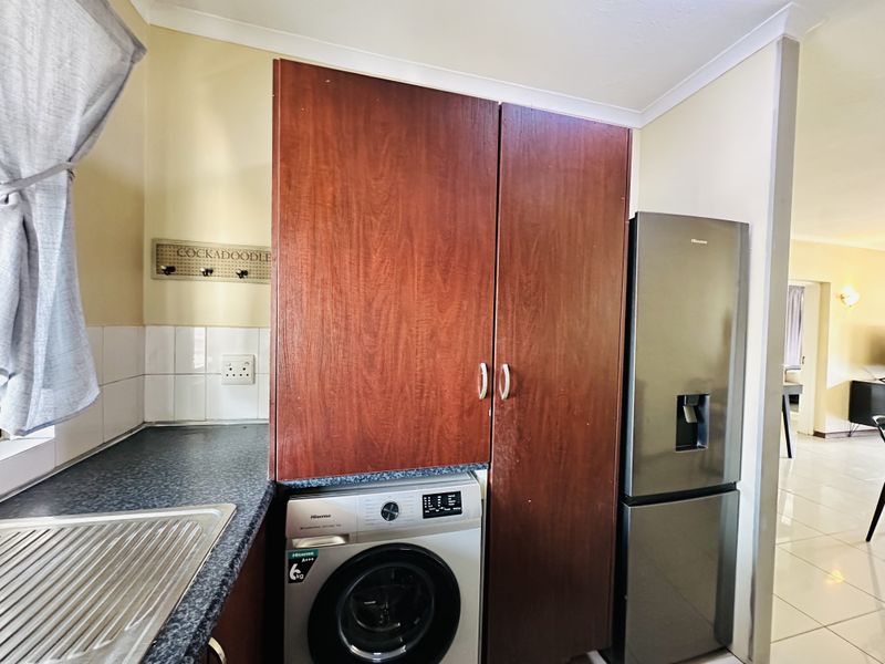 A functional laundry area featuring built-in wooden cabinetry, a laminate countertop with a stainless steel sink, and tiled backsplash.