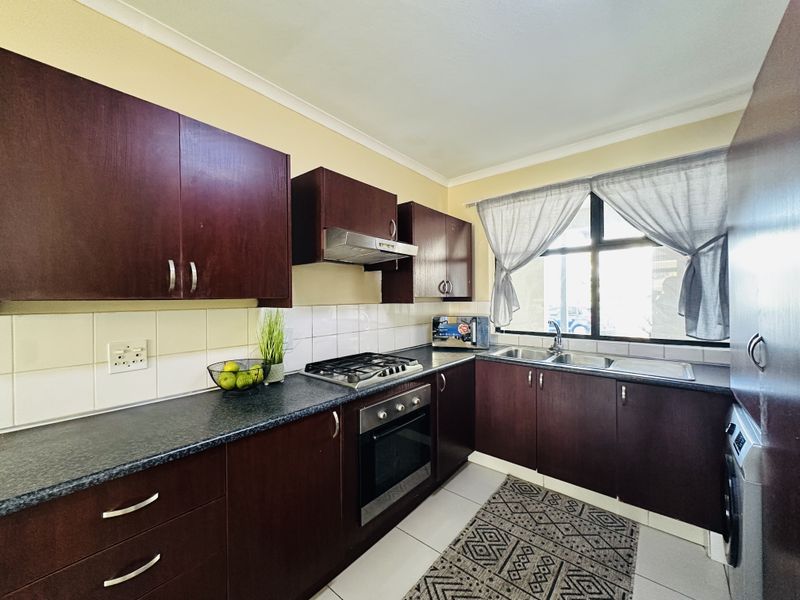 A functional kitchen featuring dark wood cabinetry, laminate countertops, a gas hob, built-in oven, and a double stainless steel sink with tiled backsplash.