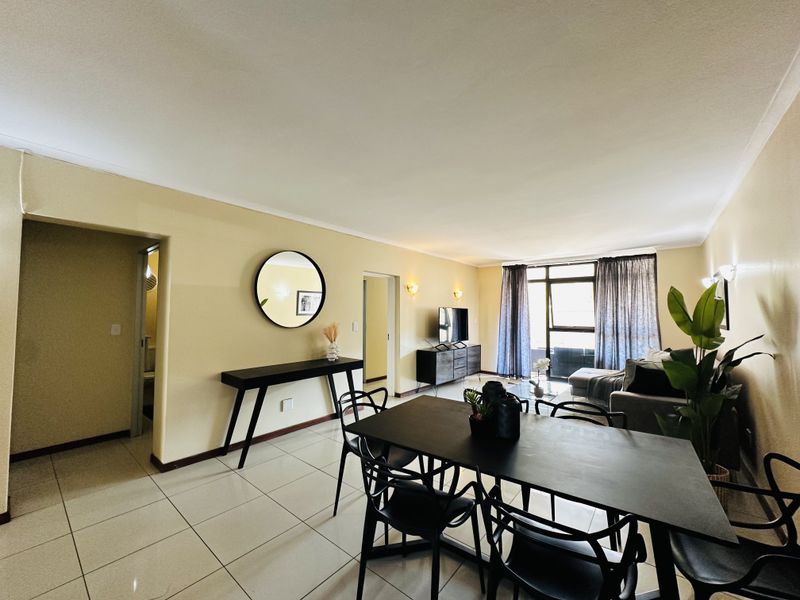 An open-plan living and dining area featuring tiled flooring, wall sconces, and a sliding glass door leading to an outdoor space.