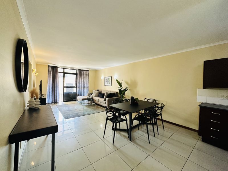 An open-plan living and dining area featuring tiled flooring, neutral walls, and direct access to an outdoor space through a sliding glass door.