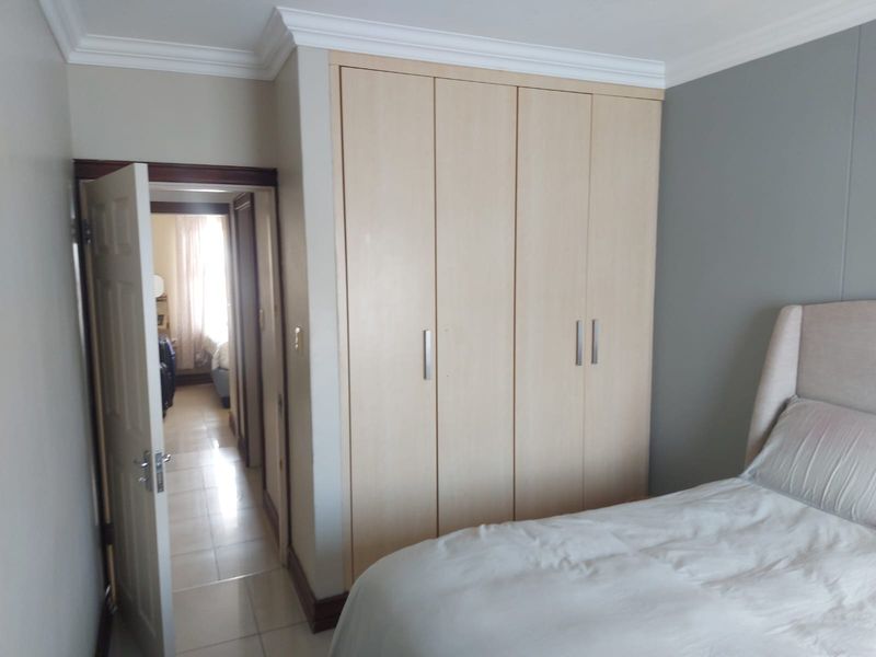 A bedroom featuring light wood built-in cupboards, crown molding, and tiled flooring, with an open doorway leading to an adjacent room.