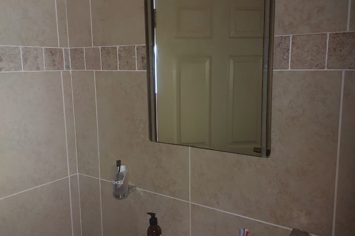 A functional bathroom featuring a wall-mounted basin with a chrome mixer tap, a wall mirror, and neutral ceramic wall tiling.