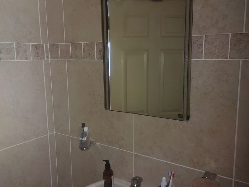 A functional bathroom featuring a wall-mounted basin with a chrome mixer tap, a wall mirror, and neutral ceramic wall tiling.