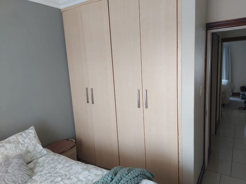 A bedroom featuring light wood-finish built-in cupboards with modern handles and tiled flooring, leading into an adjacent room.