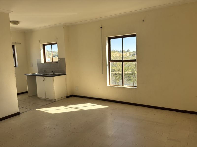 An empty open-plan living and kitchen area featuring basic cabinetry, a sink, and large windows providing natural light.