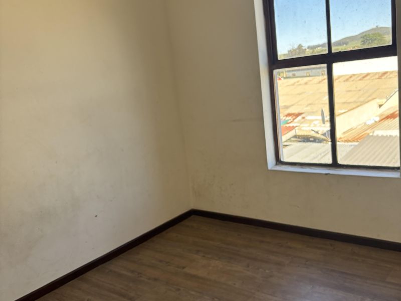 An empty bedroom featuring laminate flooring and a large window with natural light, requiring minor cosmetic attention to walls.