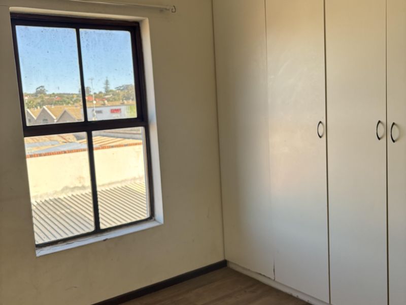 An empty bedroom featuring laminate flooring, a built-in wardrobe, and a window with a view of the surrounding neighborhood.