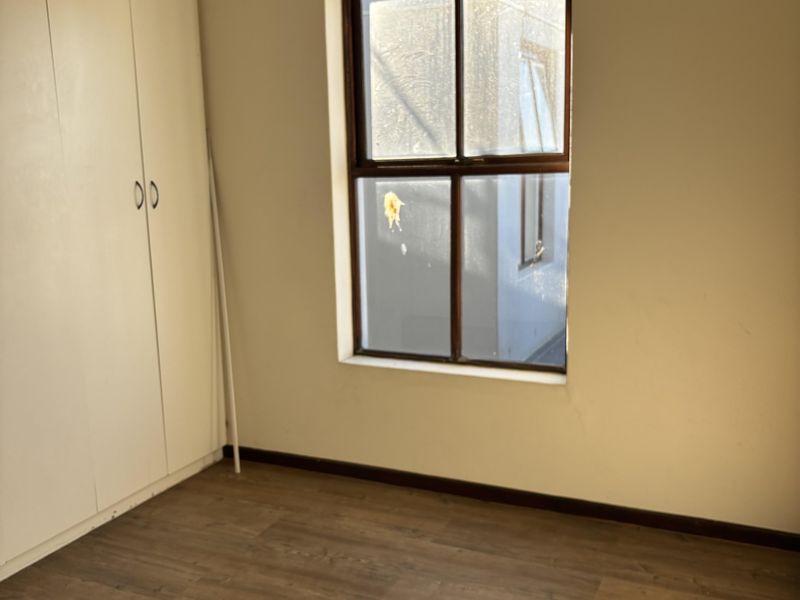 An empty bedroom featuring laminate flooring, a built-in wardrobe, and a timber-framed window with visible wall cracks.