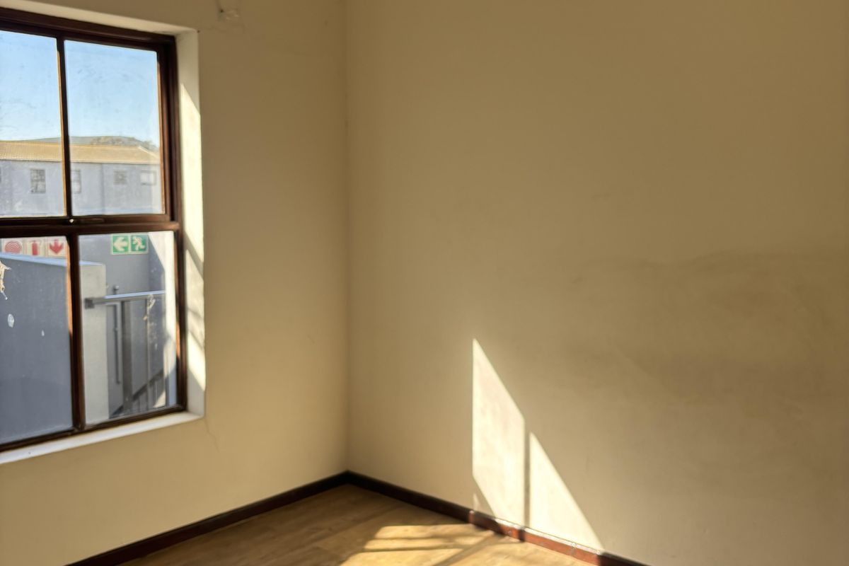 An empty bedroom featuring laminate flooring and a timber-framed window, requiring minor cosmetic repairs to walls and ceiling.