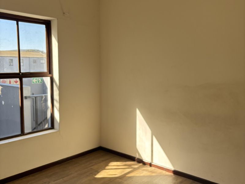 An empty bedroom featuring laminate flooring and a timber-framed window, requiring minor cosmetic repairs to walls and ceiling.
