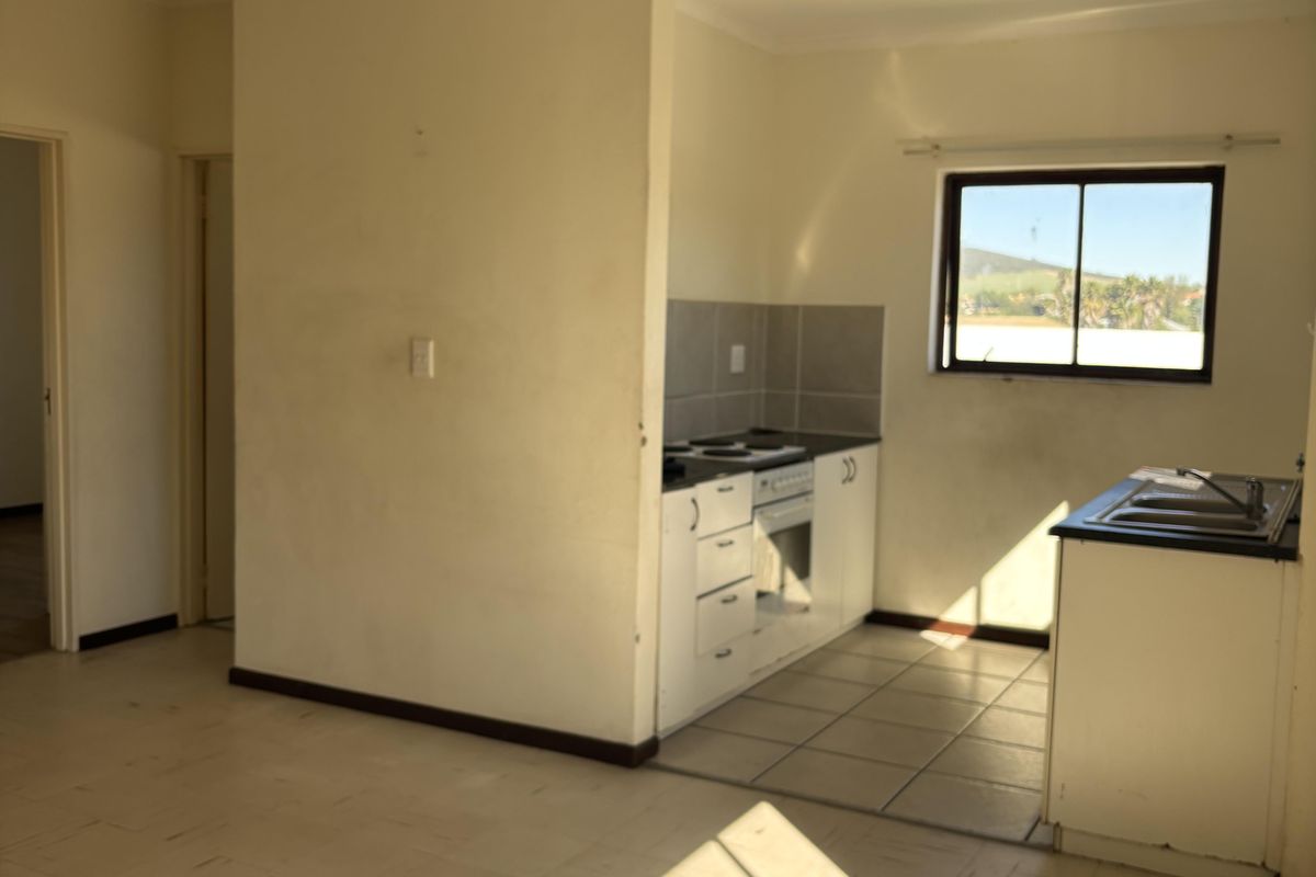 An open-plan kitchen and living area featuring dated cabinetry, built-in appliances, and tiled flooring, offering a blank canvas for renovation.