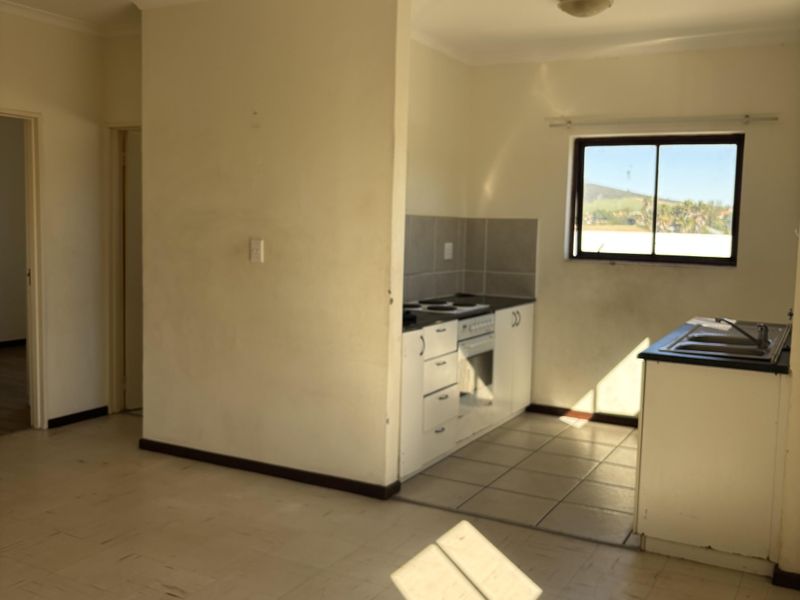 An open-plan kitchen and living area featuring dated cabinetry, built-in appliances, and tiled flooring, offering a blank canvas for renovation.