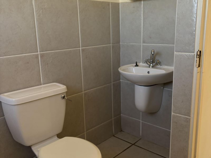A functional bathroom featuring a toilet, wall-mounted basin with mixer tap, medicine cabinet, and neutral ceramic tiling throughout.