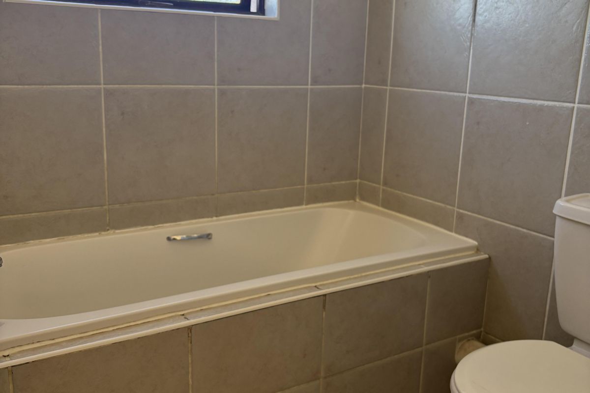 A functional bathroom featuring a built-in bathtub, tiled walls and flooring, and a standard toilet, ready for cosmetic updates.