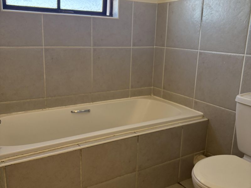 A functional bathroom featuring a built-in bathtub, tiled walls and flooring, and a standard toilet, ready for cosmetic updates.