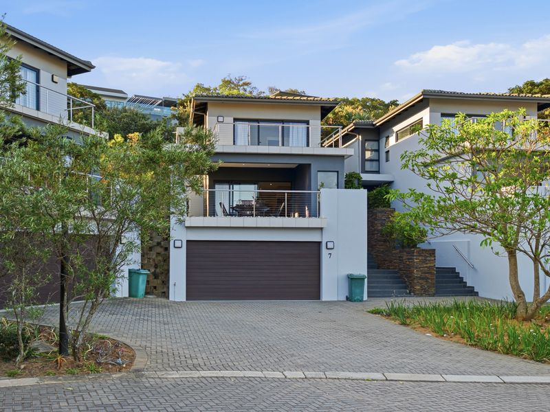Modern townhouse exterior featuring a paved driveway, double garage, and upper-level balcony with contemporary stone cladding and stainless steel balustrades.