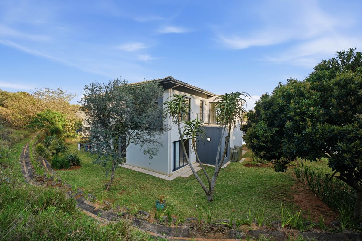 Rear view of the townhouse featuring a private garden, balcony access, and modern exterior finishes set within a landscaped environment.