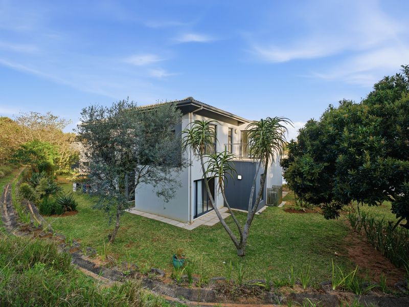 Rear view of the townhouse featuring a private garden, balcony access, and modern exterior finishes set within a landscaped environment.